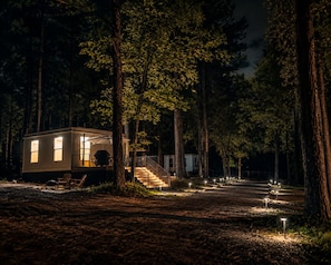 A small cabin with a porch and steps leading up to it, surrounded by trees.