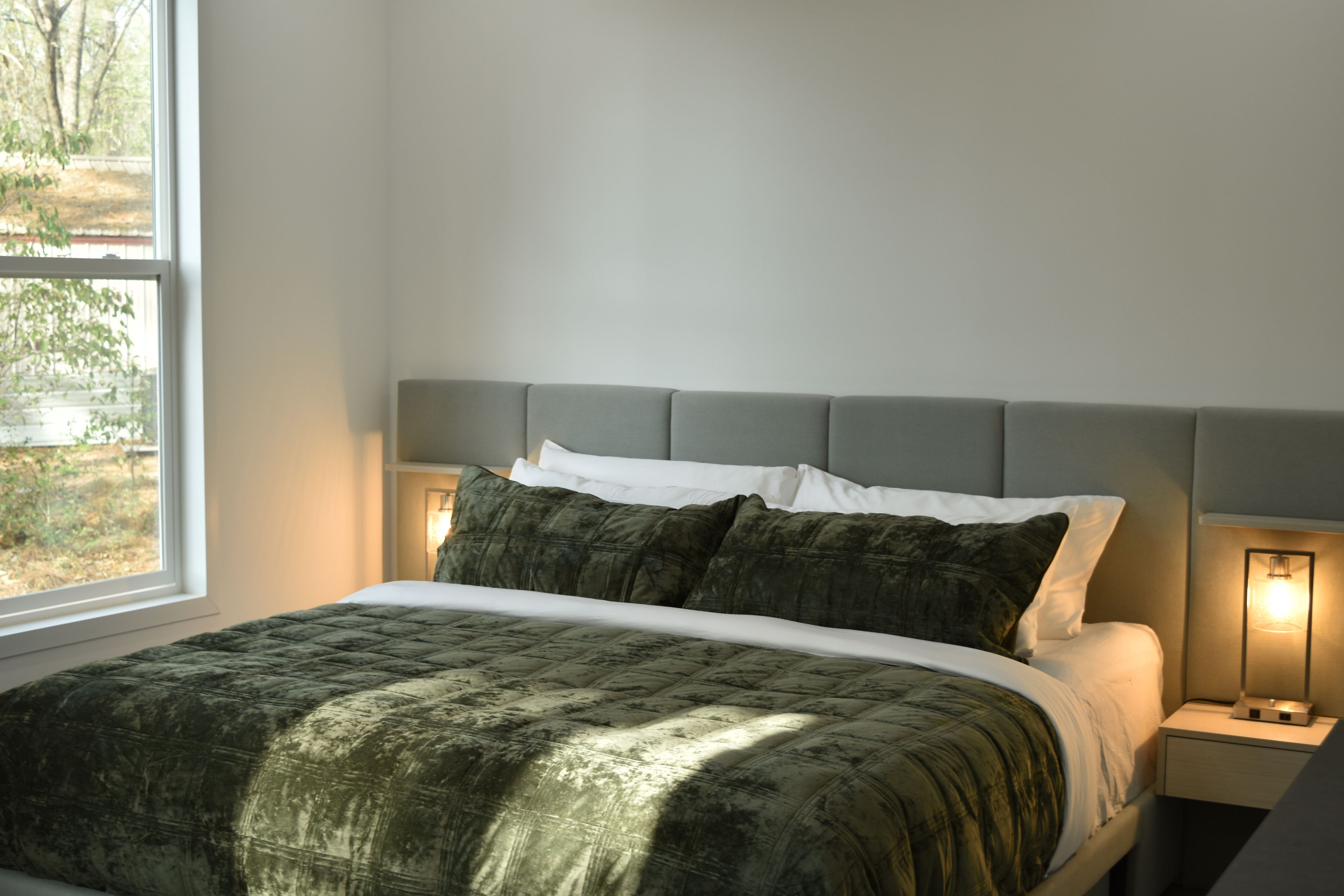 A bed with a quilted green cover, a grey headboard, and two bedside lamps.