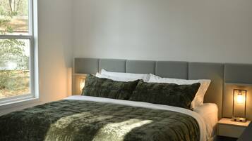 A bed with a quilted green cover, a grey headboard, and two bedside lamps.
