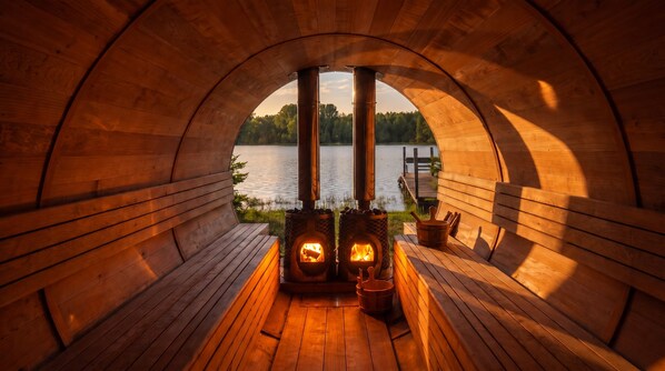 Una sauna de madera con fuego encendido en su interior, rodeada de bancos y vista a un lago.