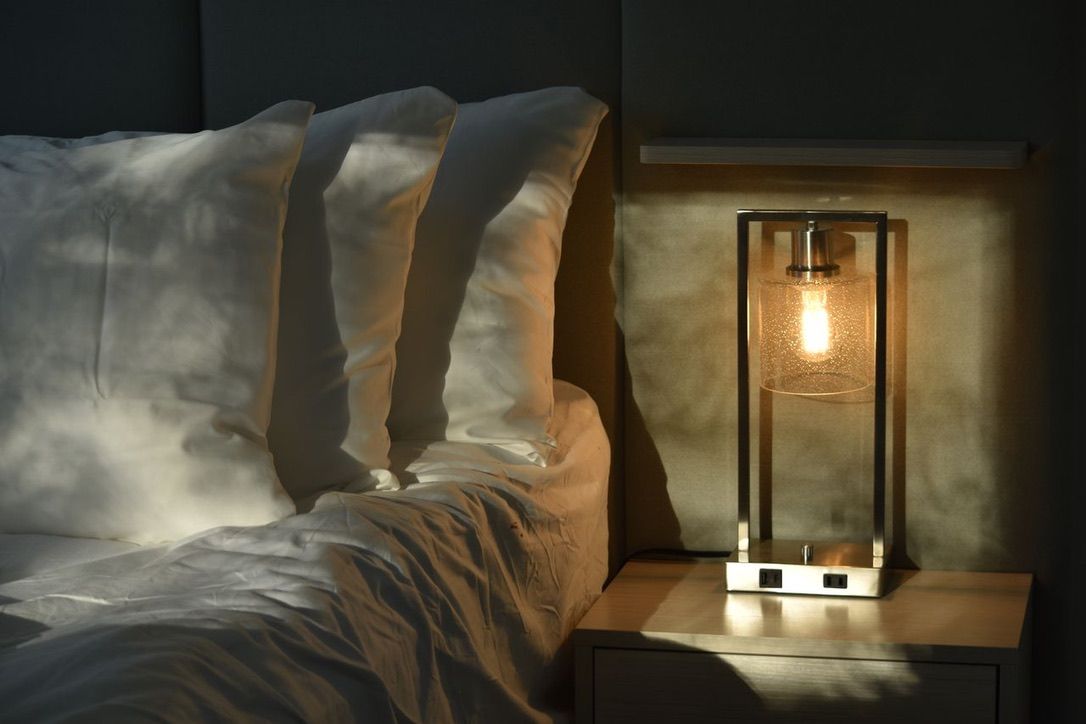 A bed with white linens and a nightstand with a lamp.