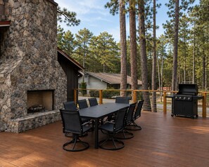 A spacious shared gathering deck with a fireplace, dining table, and grill. - Forest Villa at Horizons Sandhills (Patrick)