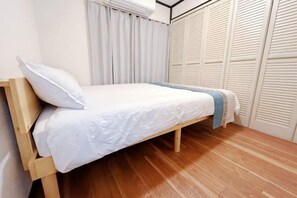 A single bed with a wooden frame and white bedding in a room with wooden flooring and white closet doors. - Hakushin no sha (Osaka)