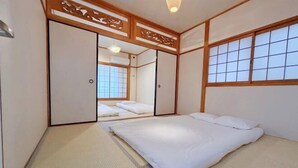 A traditional Japanese-style room with tatami flooring, a futon bed, sliding doors, and a view through a shoji screen. - Hakushin no sha (Osaka)