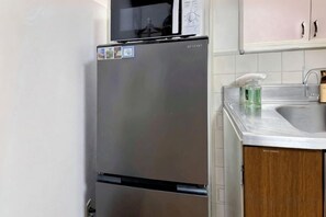 Een koelkast van roestvrij staal met daarboven een magnetron, een spoelbak met een zeepdispenser, en houten keukenkastjes.