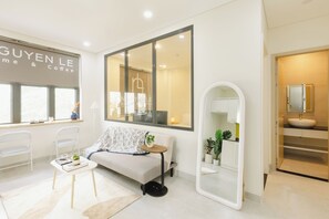 A modern hotel room with a sofa, a small table with a plant, a large mirror, and a window with a view of the outside. - Nguyen Le Pearl Central Saigon District 1 (Ho Chi Minh City)