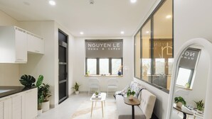 Een moderne keuken met witte kastjes, een aanrecht en een raam met uitzicht. In de woonruimte staat een bank, een klein tafeltje en een potplant.