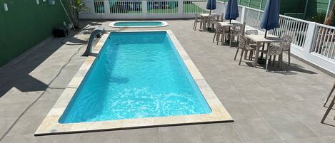 Una piscina rectangular con un borde empedrado, rodeada por una valla blanca.