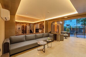 A modern lounge area with a sofa, a small table, and a glass partition. - Hotel Maskan Surat (Surat)