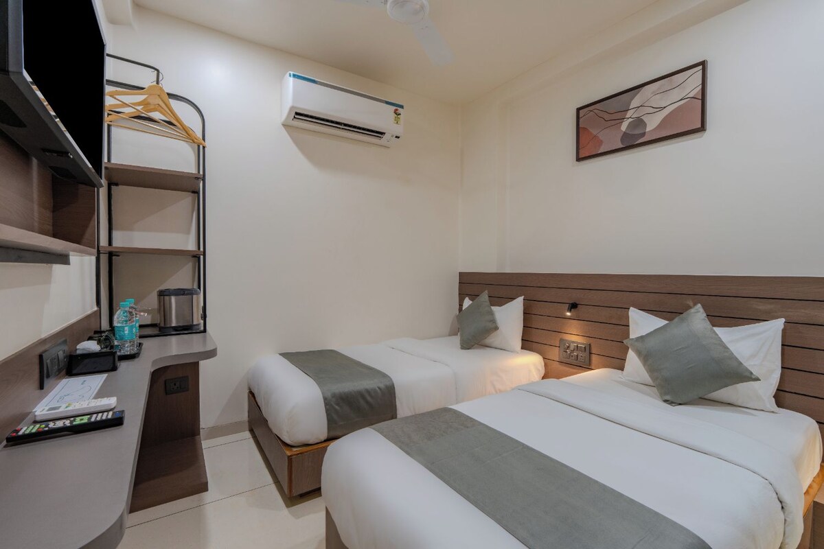 A hotel room with two beds, a desk with a computer, a water bottle, a kettle, and a painting on the wall.