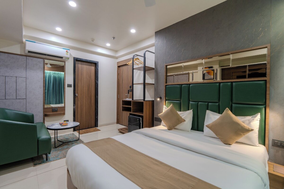 A hotel room with a large bed, a green sofa, a small table, and a wardrobe.