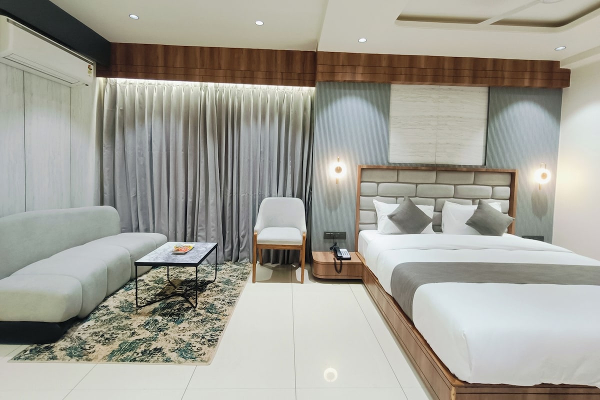 A modern hotel room with a large bed, a sofa, a small table, and a chair.