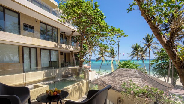 A balcony with a glass barrier, a table with fruit, and a view of the ocean and palm trees. - Encantada Residences (Boracay Island)