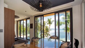 A spacious dining area with a large glass table, wicker chairs, and a view of the ocean through large windows. - Encantada Residences (Boracay Island)