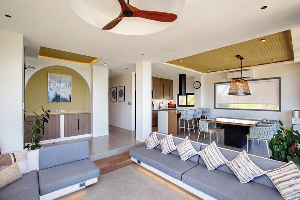 A modern living room with a grey sofa, a dining area with a bar, and a kitchen in the background. - Encantada Residences (Boracay Island)