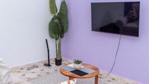 A living room with a large potted plant, a small table with a decorative item, and a mounted TV on the wall. - Grace's cozy one bedroom Kilifi apartment (Kilifi)