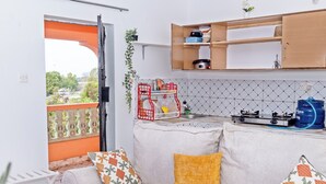 A living area with a sofa, cushions, a kitchen with a gas stove, a hanging plant, and a balcony with a railing. - Grace's cozy one bedroom Kilifi apartment (Kilifi)