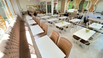 Un comedor amplio con varias mesas y sillas, un largo banco acolchado a lo largo de una pared, y elementos decorativos como espejos y paneles con diseños.