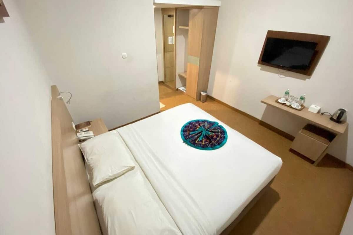 Une chambre d’hôtel avec un lit, un bureau avec une télévision et une petite salle de bain.