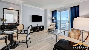 A modern living room with a dining area, a flat-screen TV, and a large window with a city view. - MGM Signature-1Br Work Desk Sphere Balcony Suite (Las Vegas)