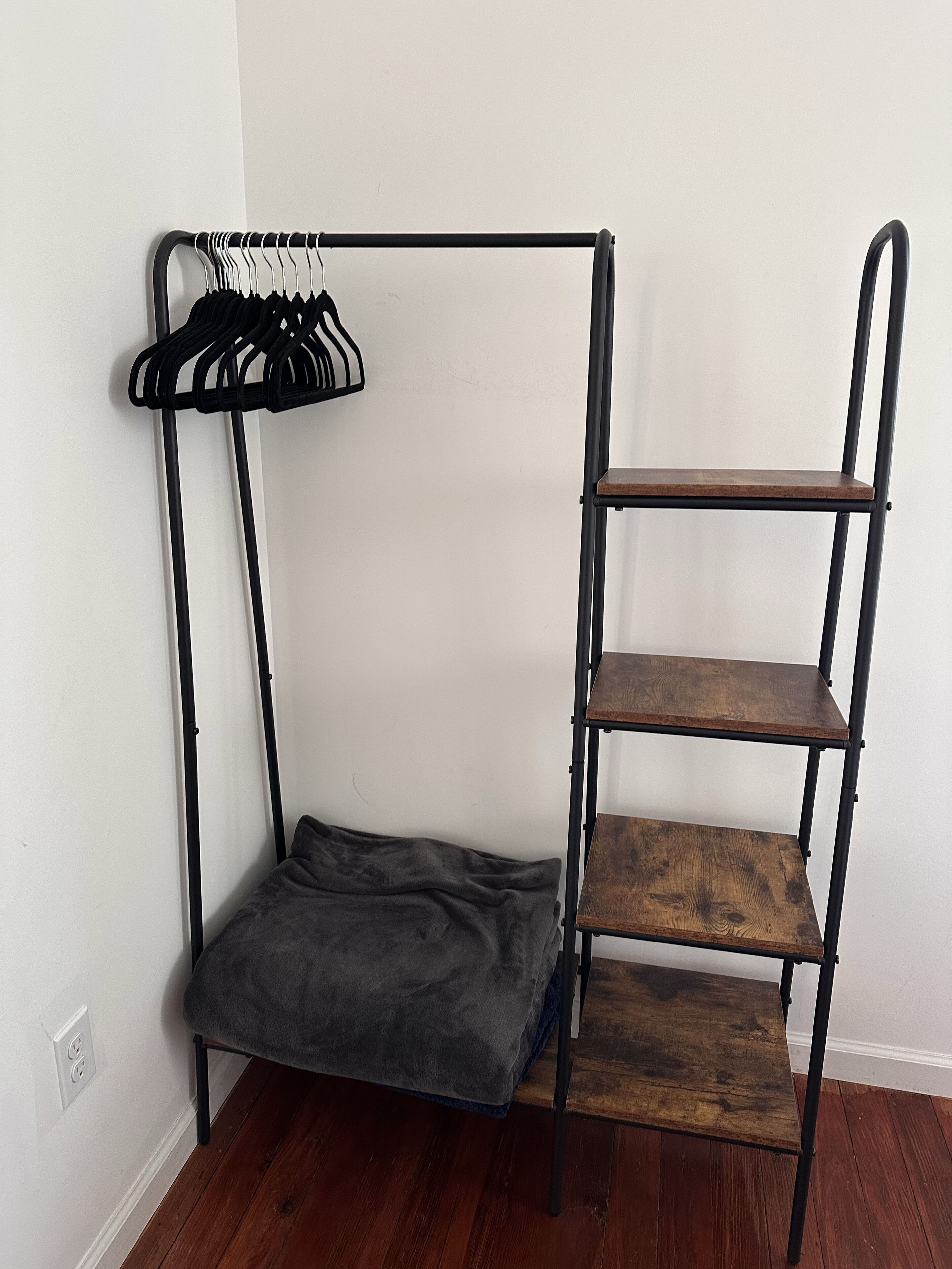 Ein Eckzimmer mit einem Metallstockbett, einer Holzregaleinheit und einem grauen Kissen.