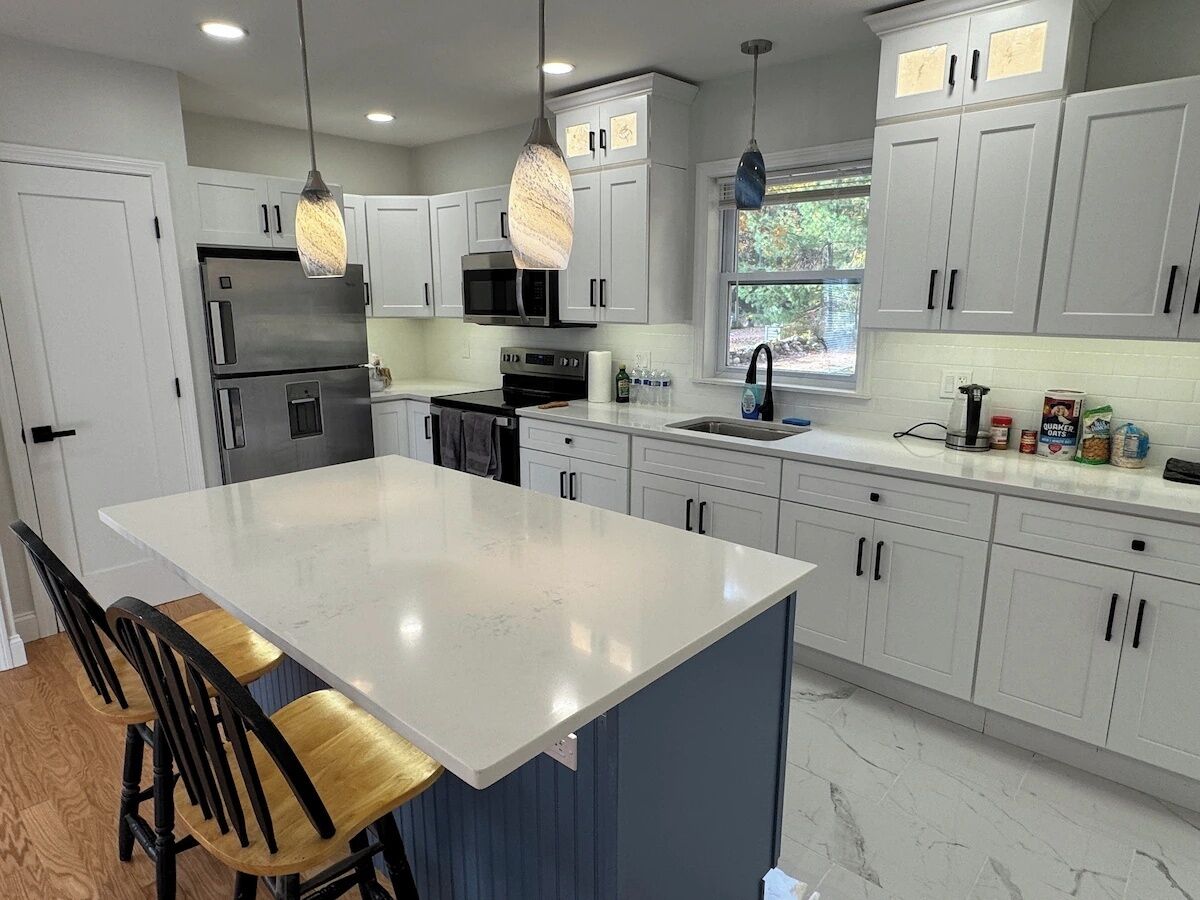 Une cuisine moderne avec des meubles blancs, un grand îlot central, des appareils en acier inoxydable et des luminaires suspendus.