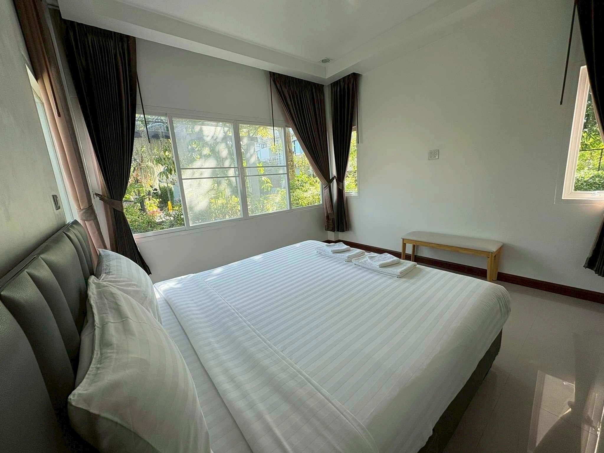 A hotel room with a large bed, a bench, and a window with curtains.