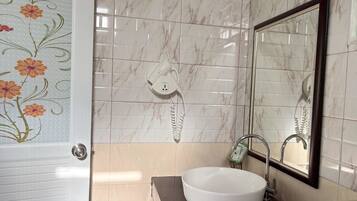 A bathroom with a white marble tiled wall, a white sink, a handheld hair dryer, and a mirror.