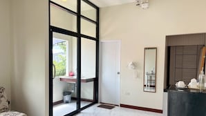 Ein Hotelzimmer mit einer großen Schiebeglasdoor zum Balkon, einem kleinen Waschbecken, einem Telefon und einem Spiegel an der Wand.