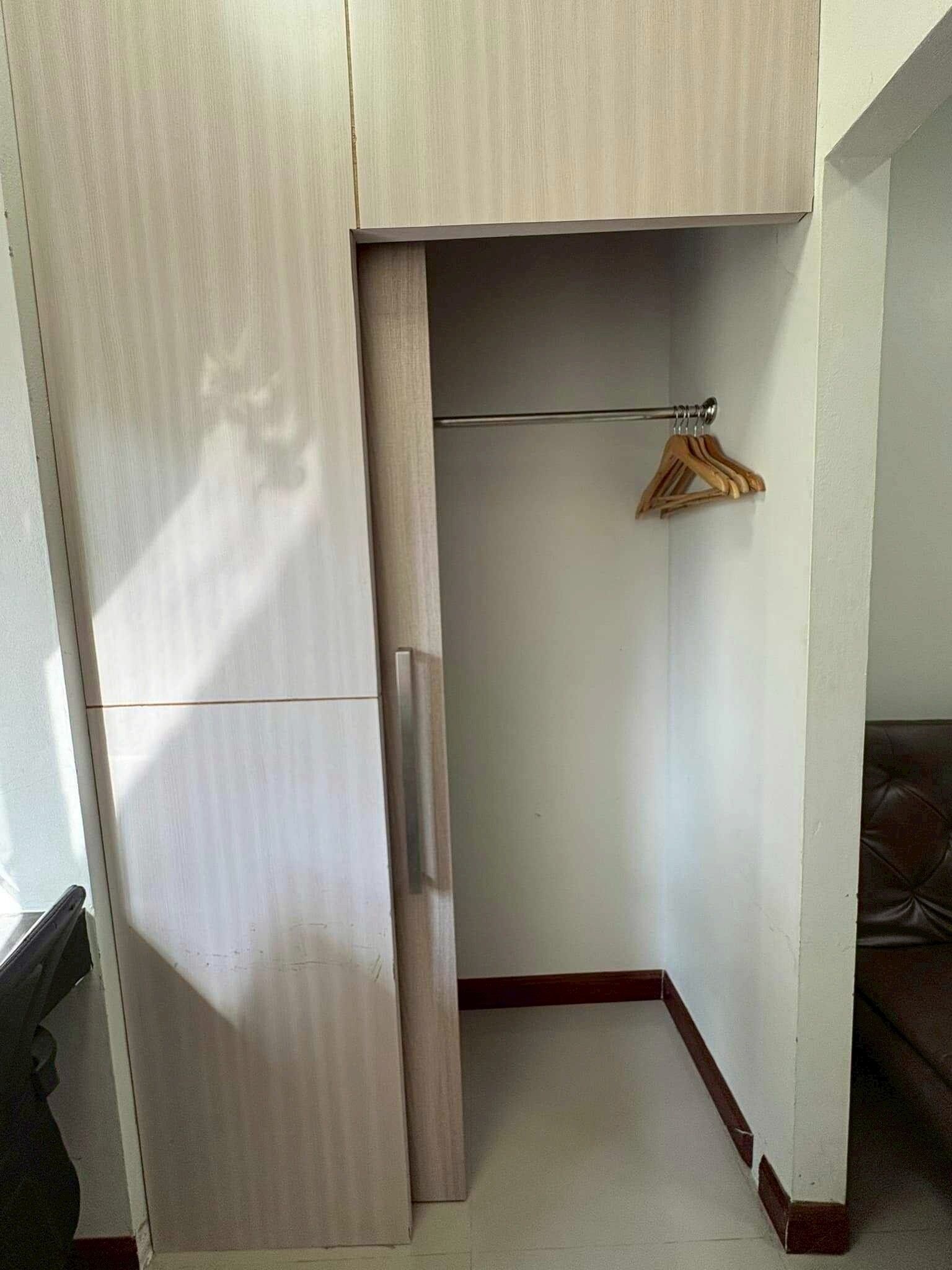 A corner of a room with a wooden wardrobe, a hanging rod with wooden hangers, and a brown leather sofa.