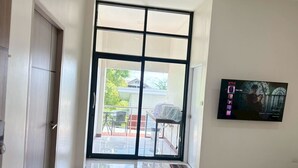 Ein modernes Interieur mit einer Schiebeglastür, die auf einen Balkon führt, einem am Wand montierten Fernseher, der einen Film zeigt, und einem sauberen, gefliesten Boden.