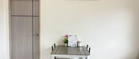 Una habitación con puerta de madera, una pequeña mesa con dos sillas, un cuadro enmarcado en la pared y una cama con cubrecama estampado.
