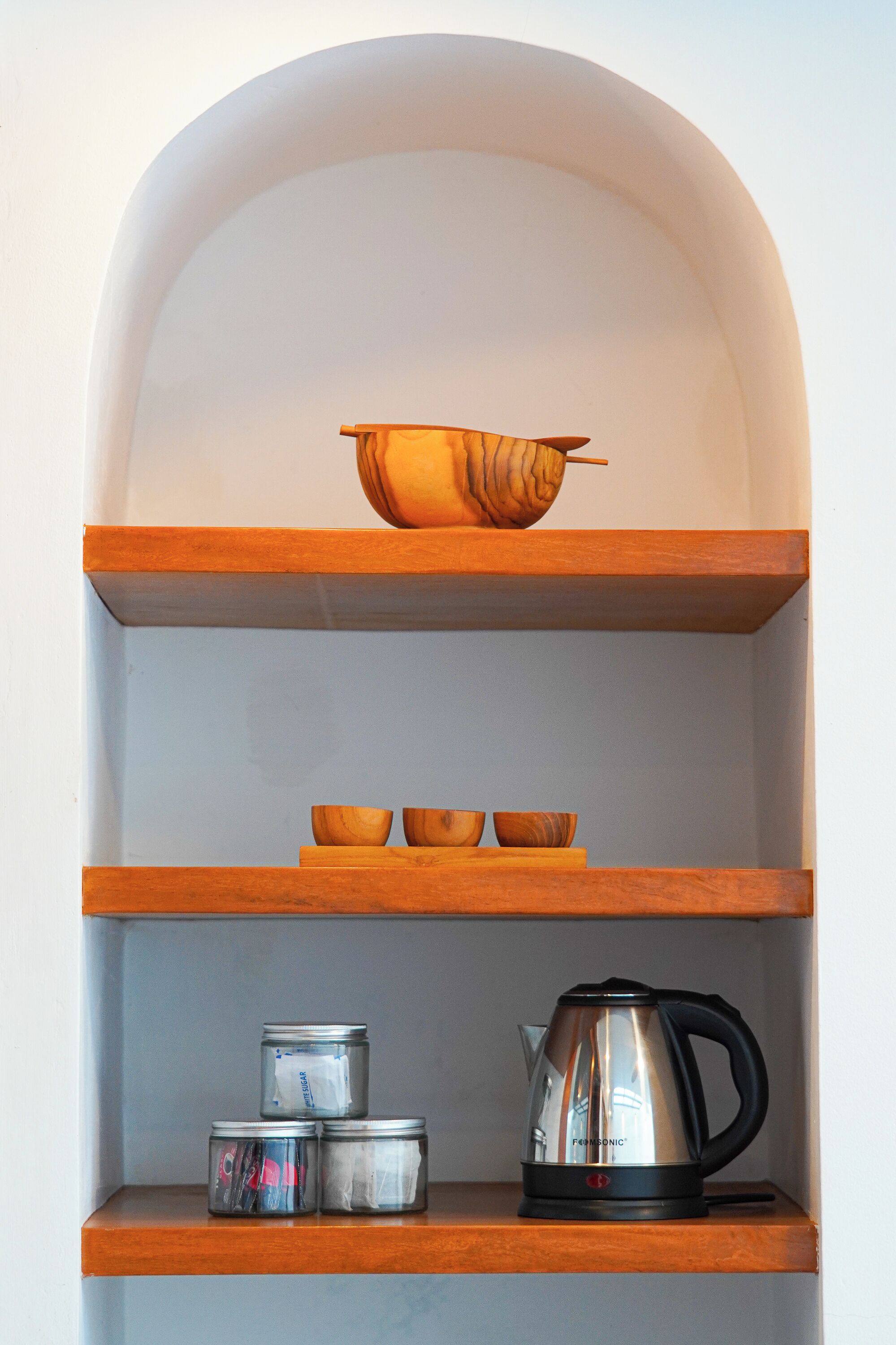 A kitchen shelf with a bowl, three small containers, and a kettle.