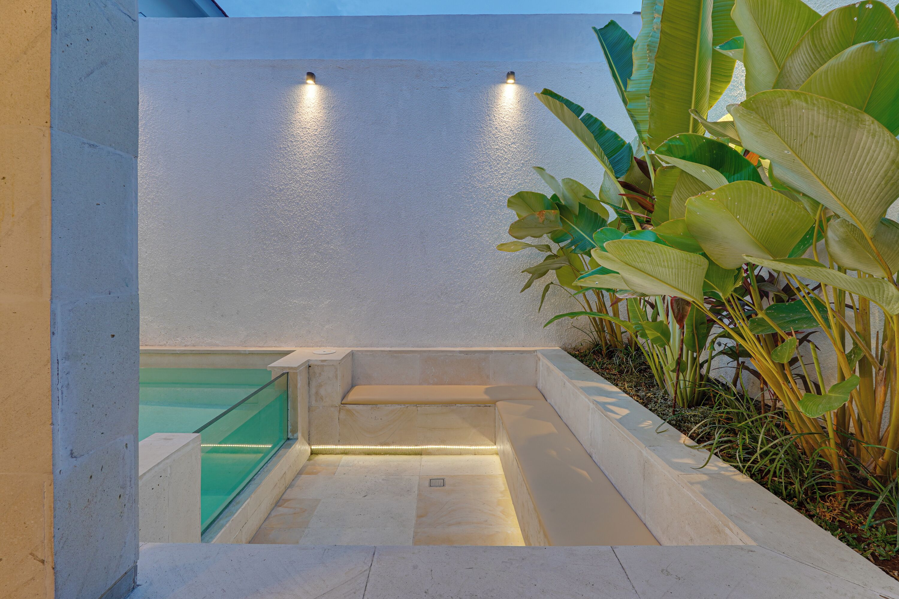 A modern outdoor seating area with a bench, a glass railing, and a planter with large green leaves.