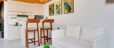 Una sala de estar moderna con un sofá blanco, dos sillas de madera, una mesa de centro de mármol con una planta y un ventilador de techo.
