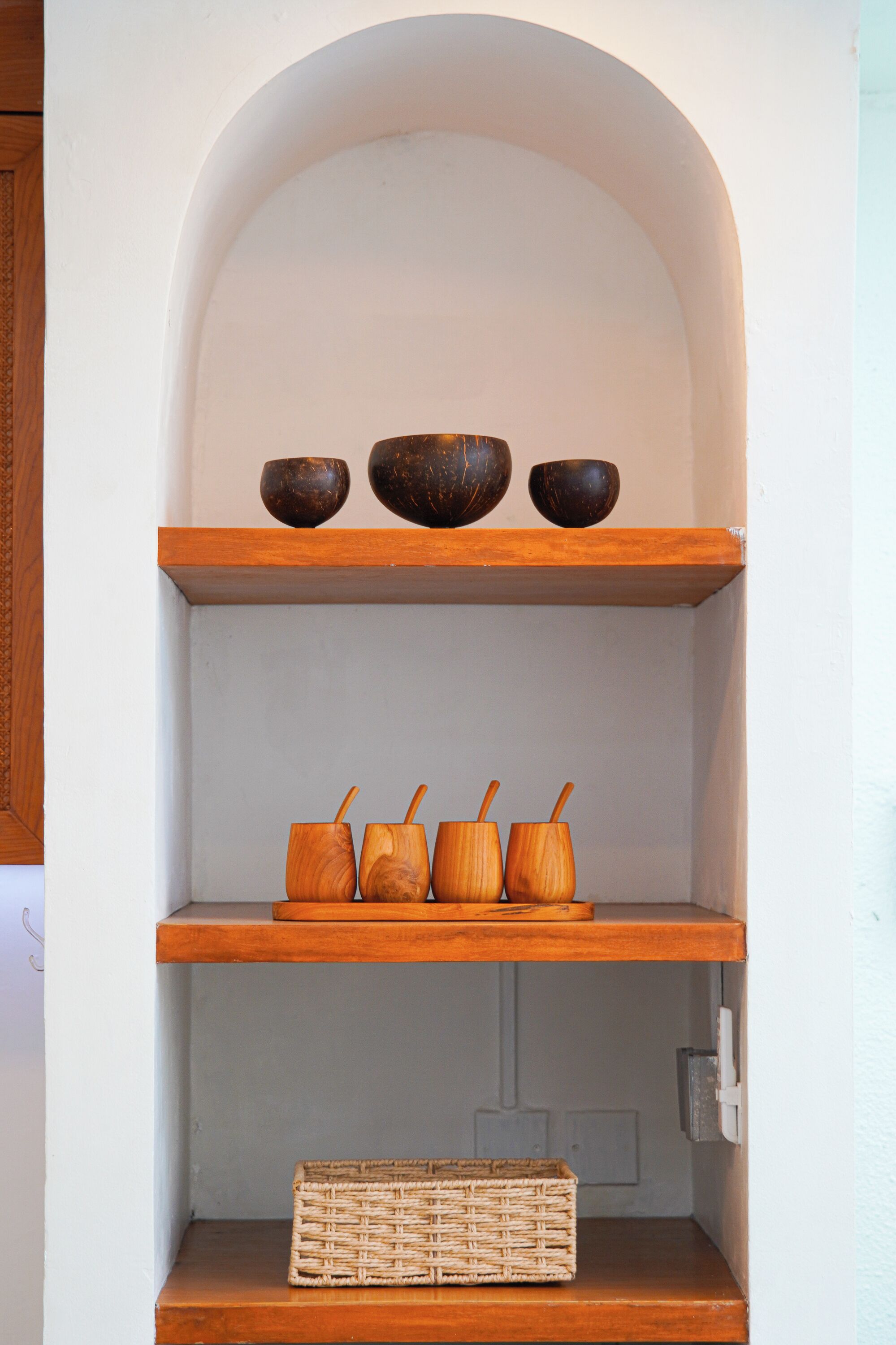 Un estante de madera con tres cuencos oscuros y cuatro tazas de madera.