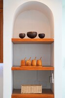 Un estante de madera con tres cuencos oscuros y cuatro tazas de madera.