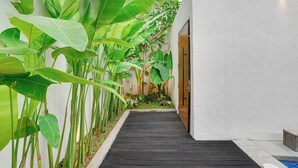Un sendero de madera estrecho que lleva a una puerta, rodeado de abundante vegetación.