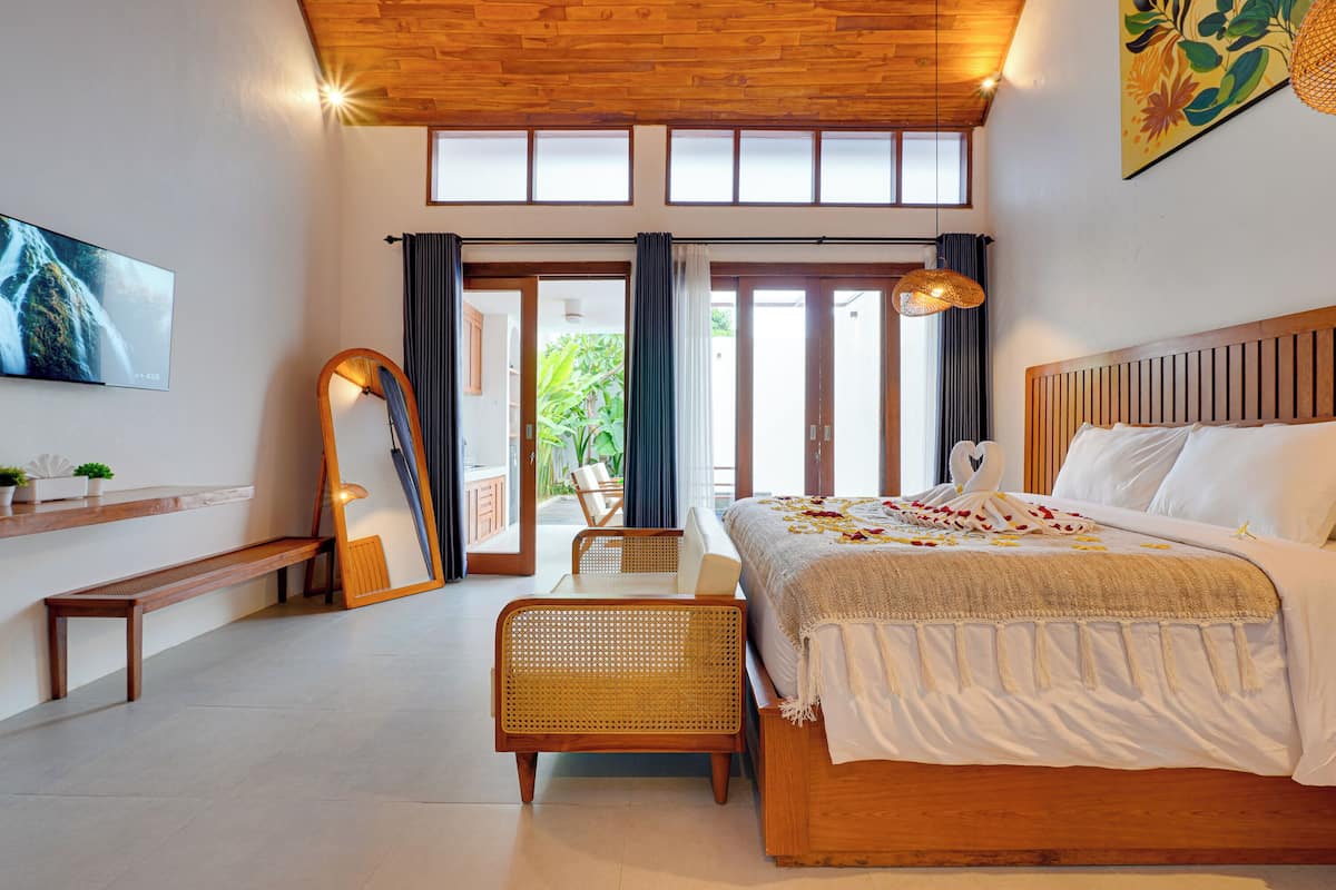 A bedroom with a bed, a bench, a chair, a TV, and a large window.