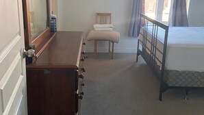 A bedroom with a bed, a dresser, a chair, and a window with curtains. - Divinity Hut (Brampton)