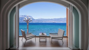 Ένα μπαλκόνι με δύο καρέκλες και ένα τραπέζι, με θέα στη θάλασσα και βουνά στο βάθος.