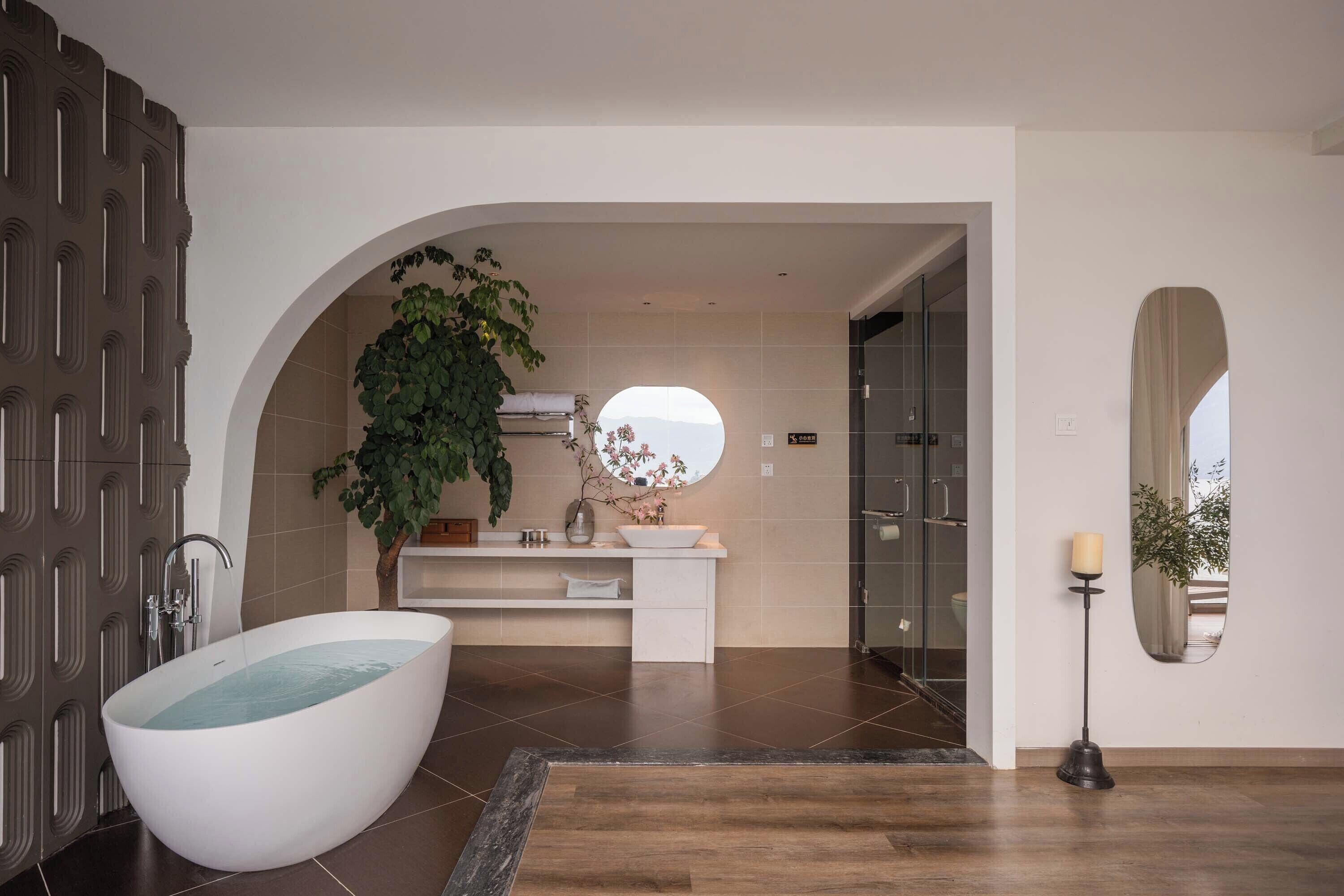A modern bathroom with a freestanding bathtub, a large mirror, and a potted plant.