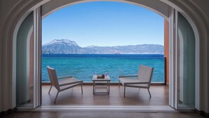 Ένα δωμάτιο με θέα στη θάλασσα και τα βουνά, που διακρίνεται μέσα από ένα τοξωτό άνοιγμα πόρτας.