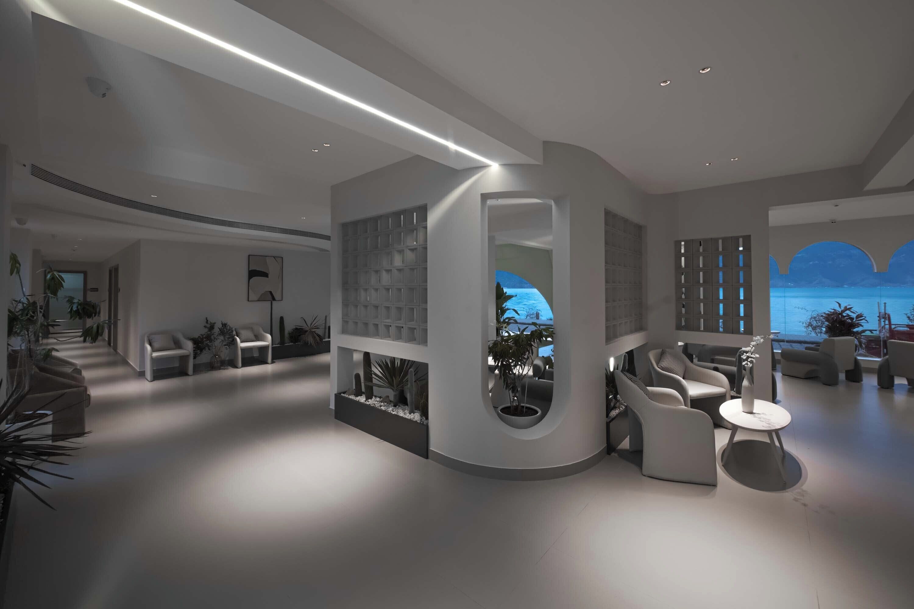 A modern interior with a curved seating area, a built-in bookshelf, and a view of the sea through a window.