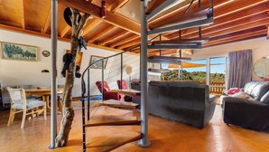 Une pièce spacieuse avec un plafond en bois, un escalier, un canapé gris et un coin repas doté de meubles en bois.