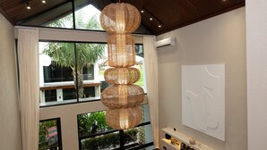 A modern interior with a large window, a decorative woven light fixture, and a minimalist wall art piece. - Adva Garden Village (Canggu)