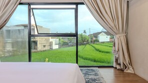 A bedroom with a large window, curtains, and a bed. - Adva Garden Village (Canggu)