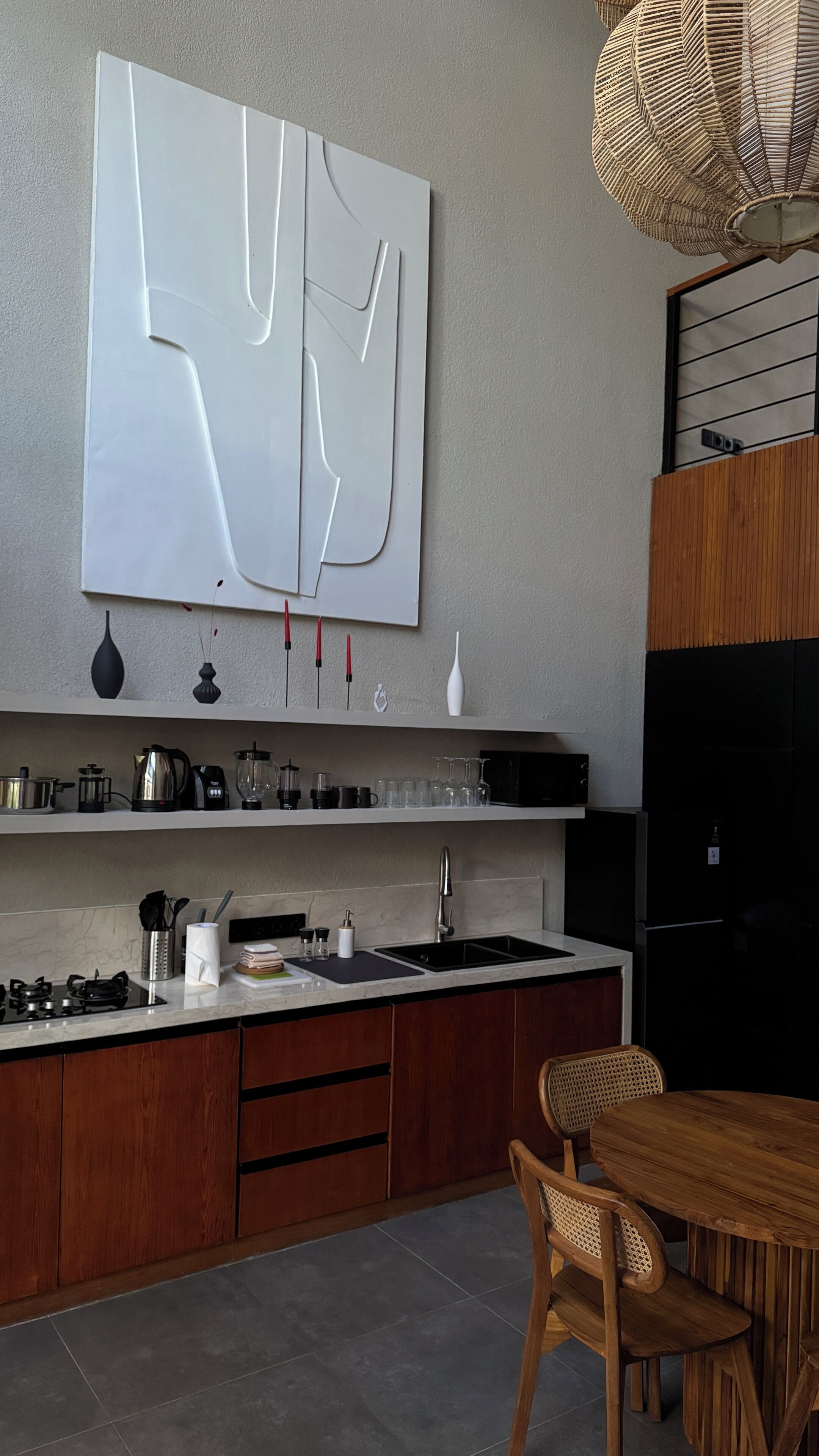 A modern kitchen with a large abstract artwork, a dining area with a wooden table and chairs, and a black refrigerator.