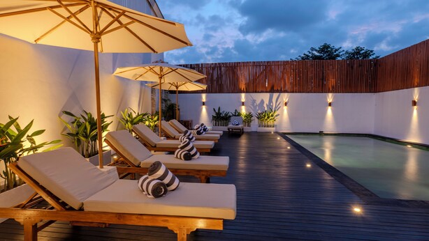 A poolside area with lounge chairs and umbrellas, surrounded by walls and potted plants. - Adva Garden Village (Canggu)