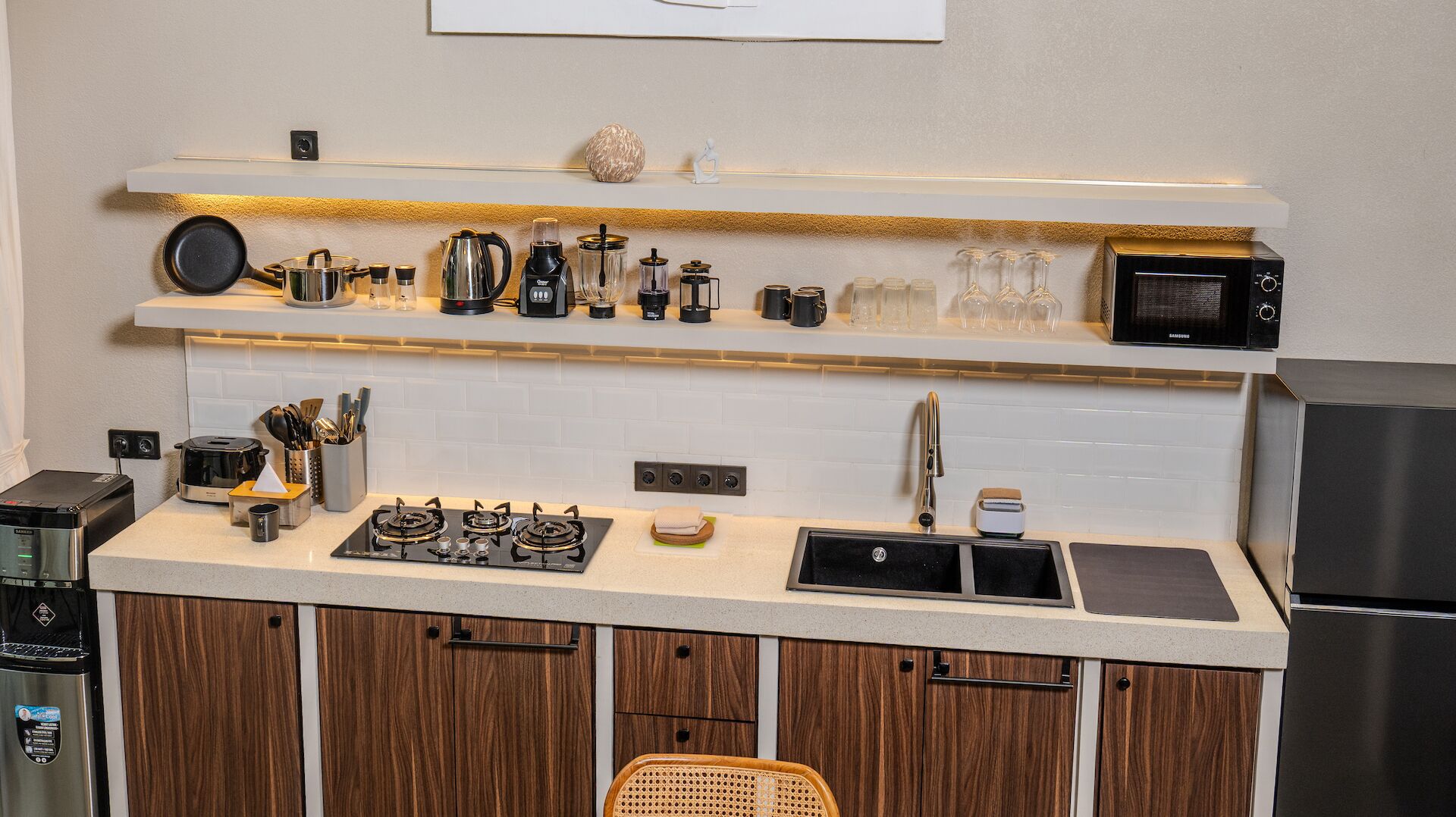 A modern kitchen with a built-in stove, a microwave, and a sink. There are shelves above the counter holding various kitchen items.